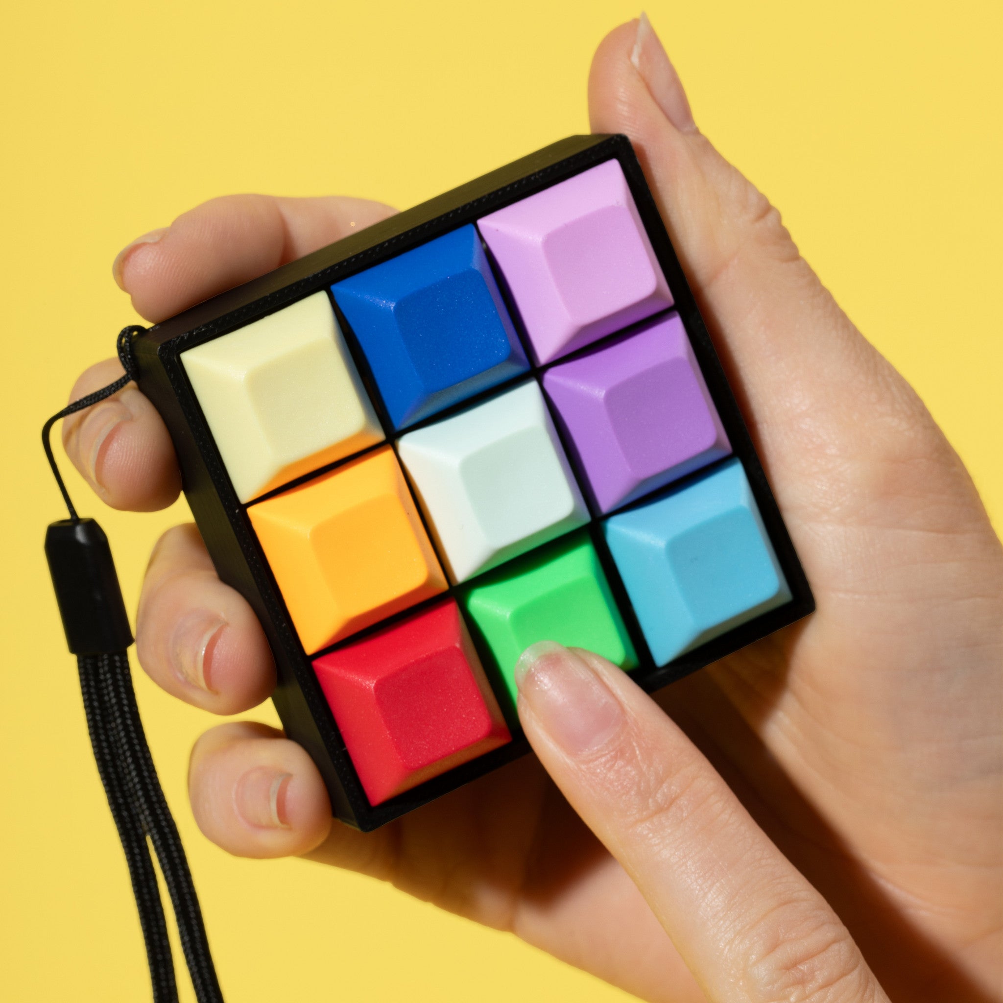 Hand holding a bright rainbow colored keyboard fidget toy on a yellow background