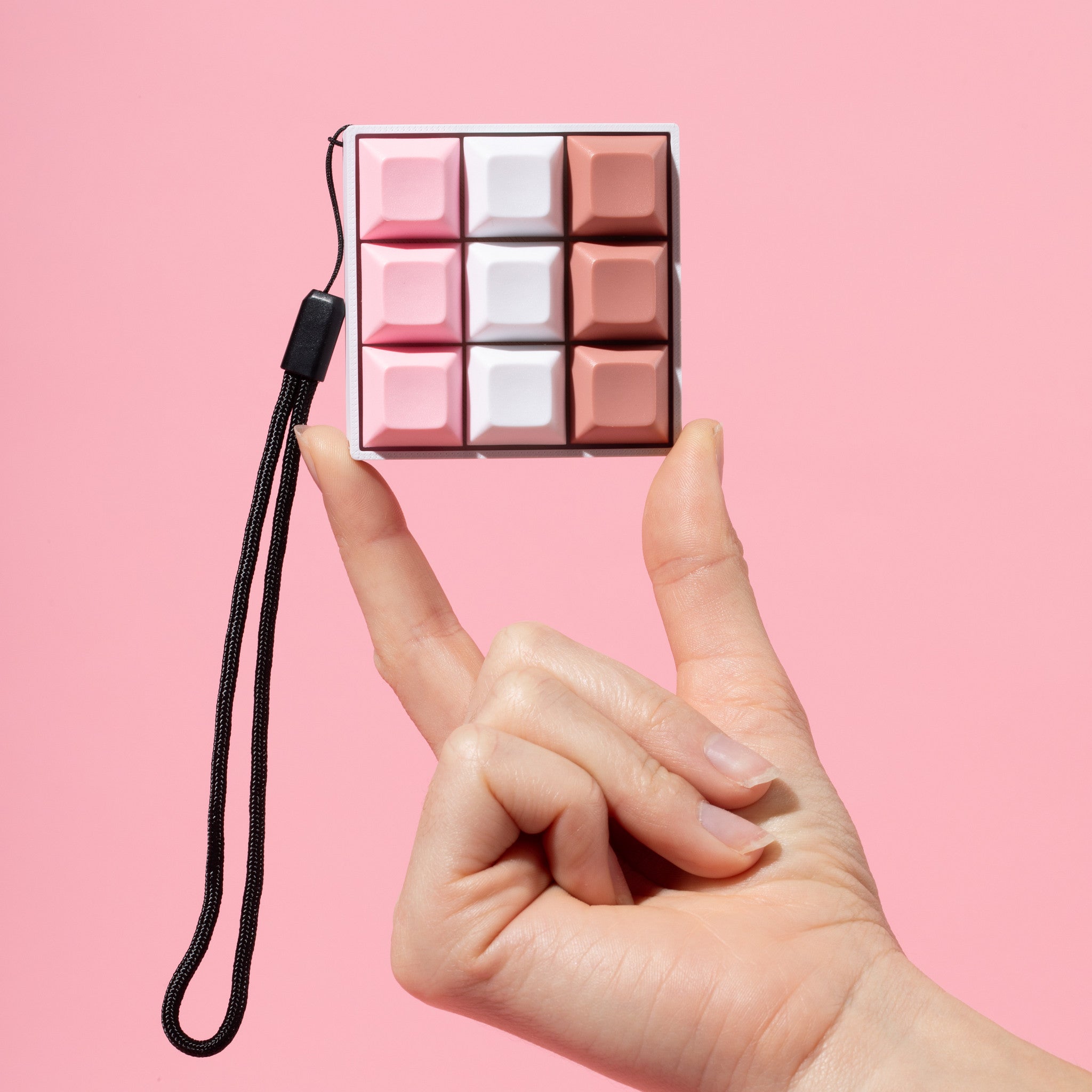 A hand holding a mechanical keyboard fidget toy with a neapolitan ice cream color theme on a pink background